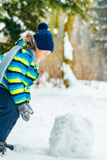 Auf dem Bild ist ein Junge zu sehen, der einen größeren Schneeball vor sich her rollt. Der Schneeball soll zeigen, wie aus Gedanken ein Glaubenssatz entsteht.